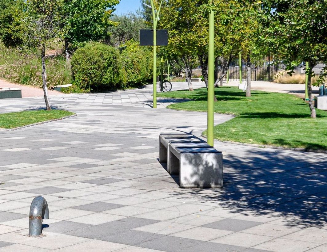 A sunny urban park path beside a modern glass office tower in Santiago, Chile.